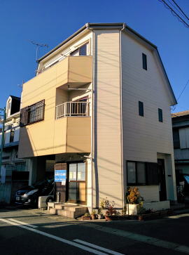 白とベージュのツートンカラー3階建ての1階がAMSパソコン教室 松戸本部です。